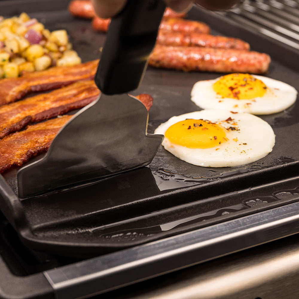 Griddle scraper blade lifting under fried eggs on the cooking surface