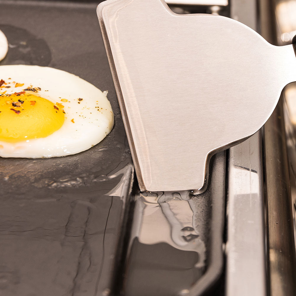 Wide metal scraper blade for griddle use with black handle and notch