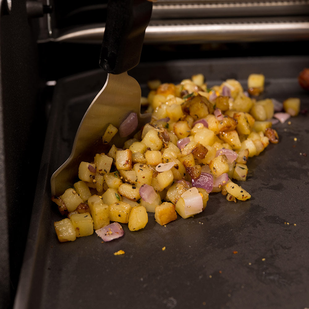 Griddle scraper lifting chopped vegetables from the cooking surface