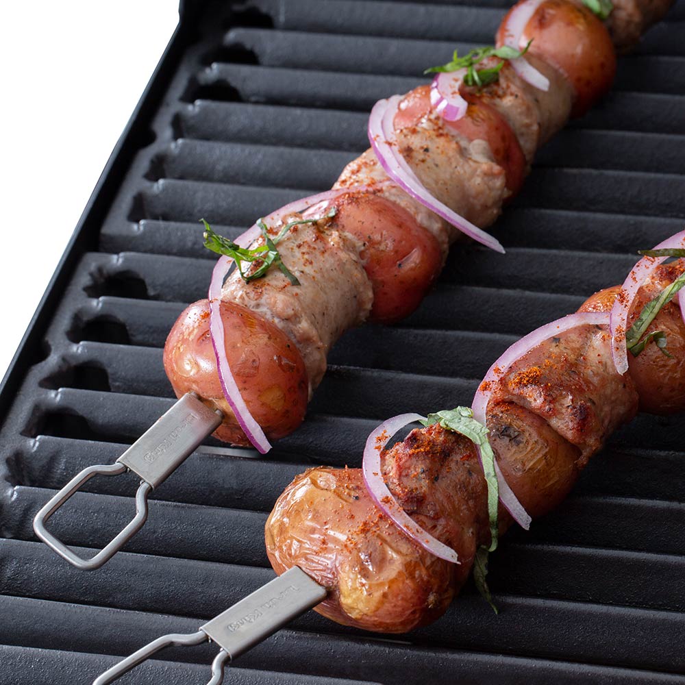 Stainless steel dual-prong skewers with sausage pieces on the grill