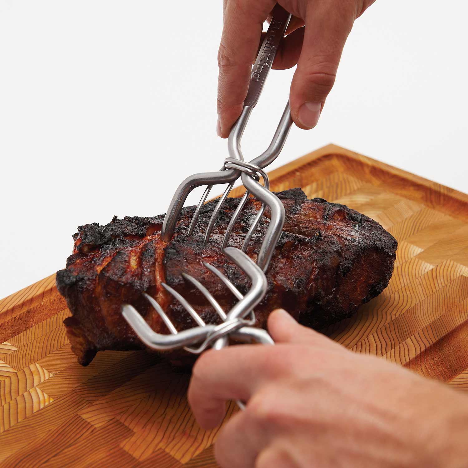 Stainless steel pork claws lifting a roast on a wooden cutting board