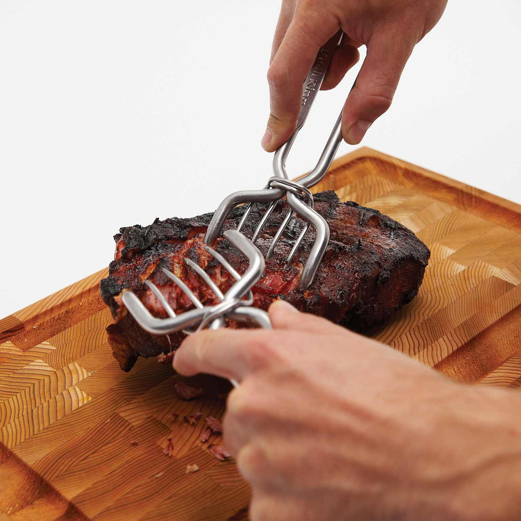 Stainless steel pork claws separating meat while held above a roast