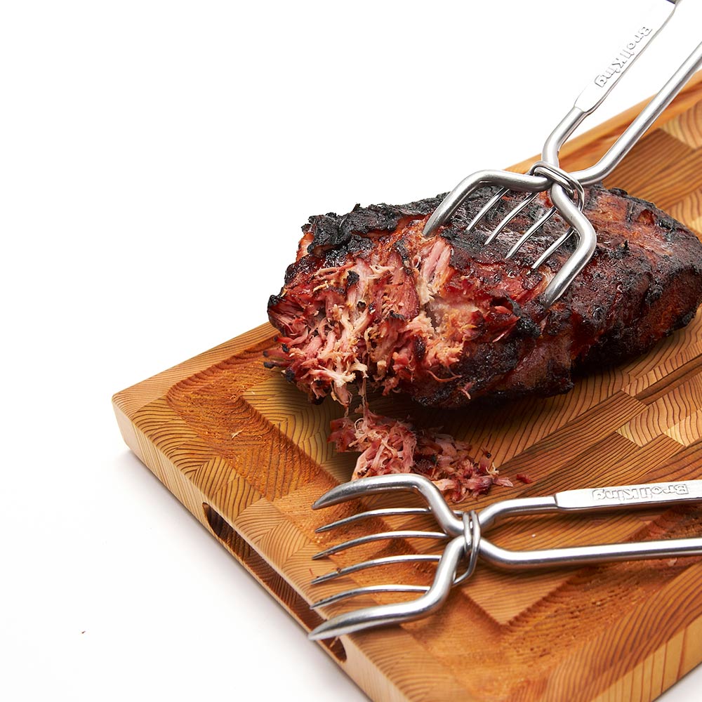 Stainless steel pork claws resting on a cutting board beside shredded meat