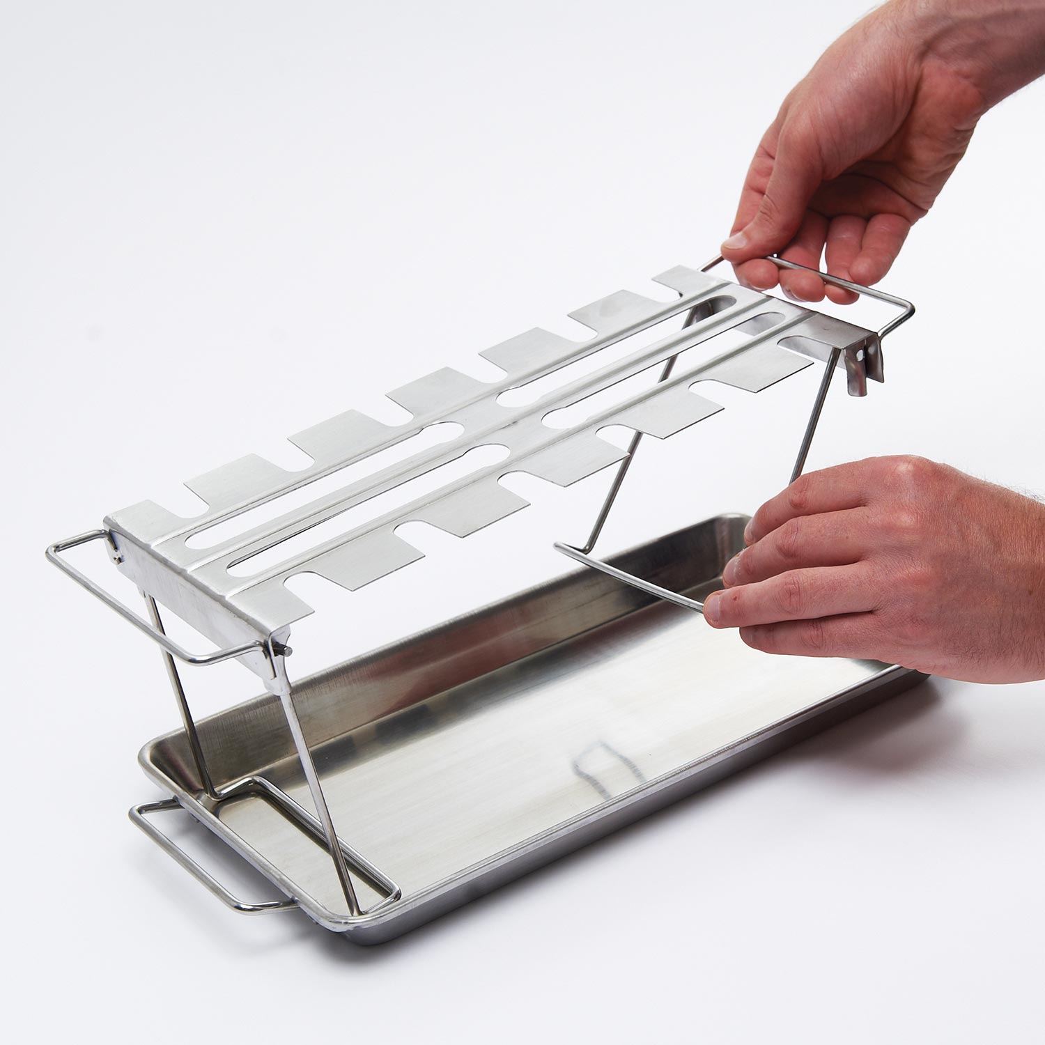 Stainless steel wing rack placed over a drip pan with support bars and lifting handle