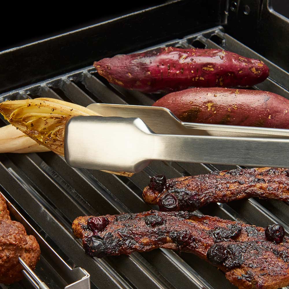 Stainless steel grill tongs holding meat on a barbecue grate