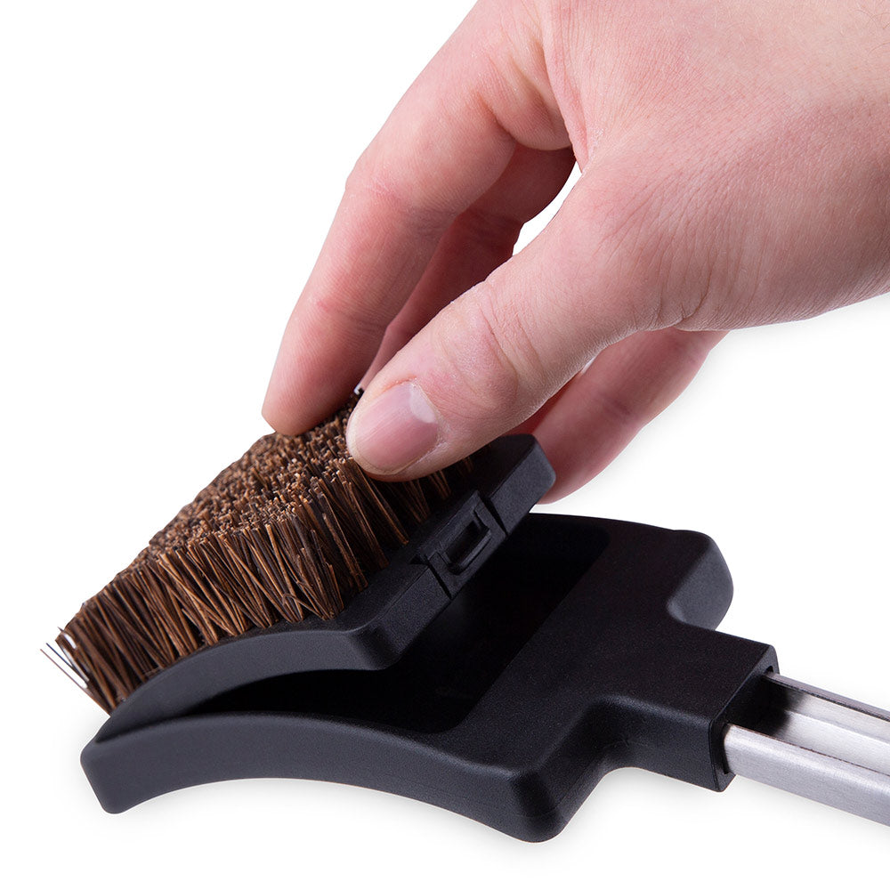 Grill brush head with copper bristles and black plastic mount, held by hand