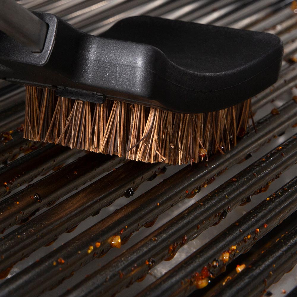 Grill brush head on metal grates, copper bristles sweeping across rails