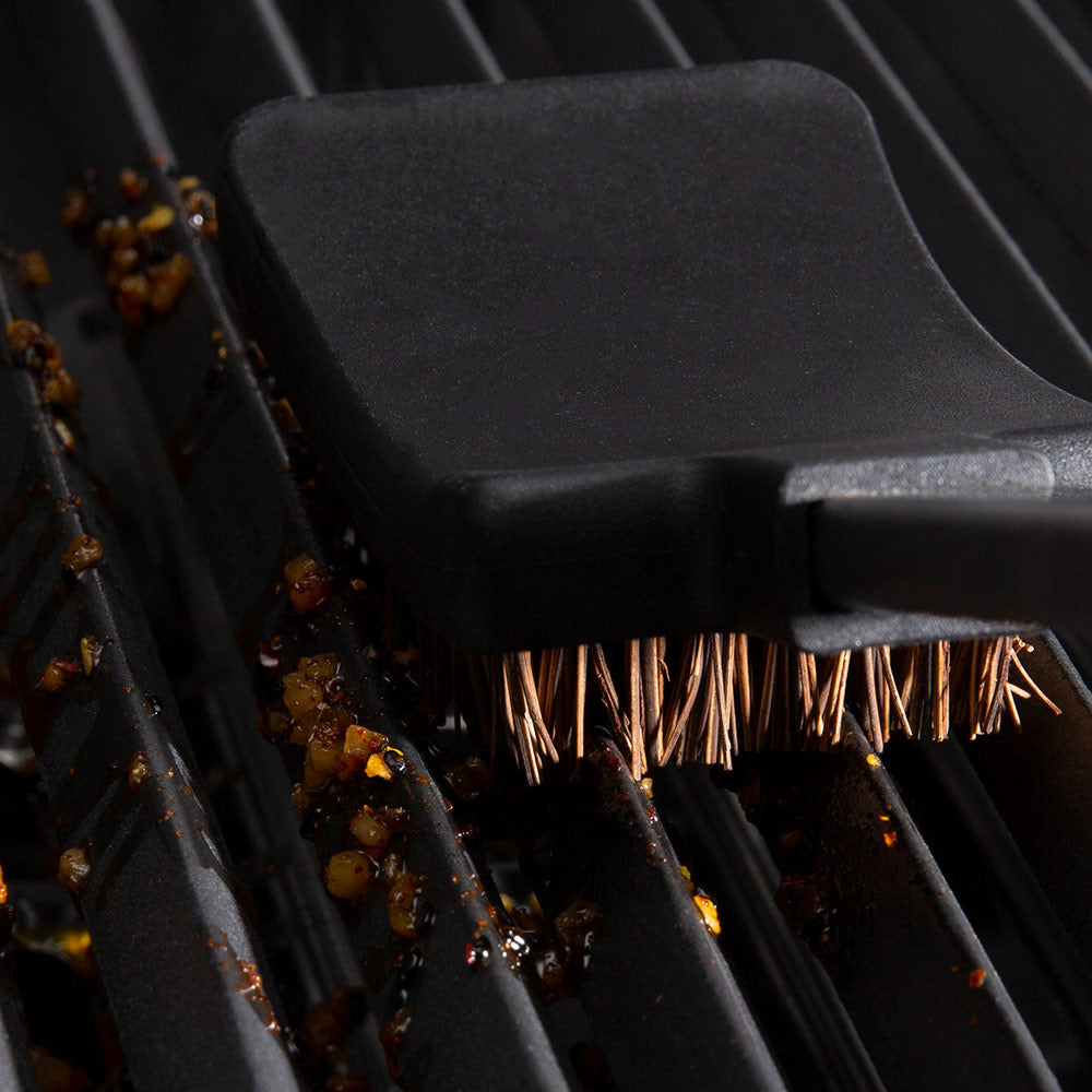 Grill brush head bristles scrubbing dirty metal grates with black plastic cover