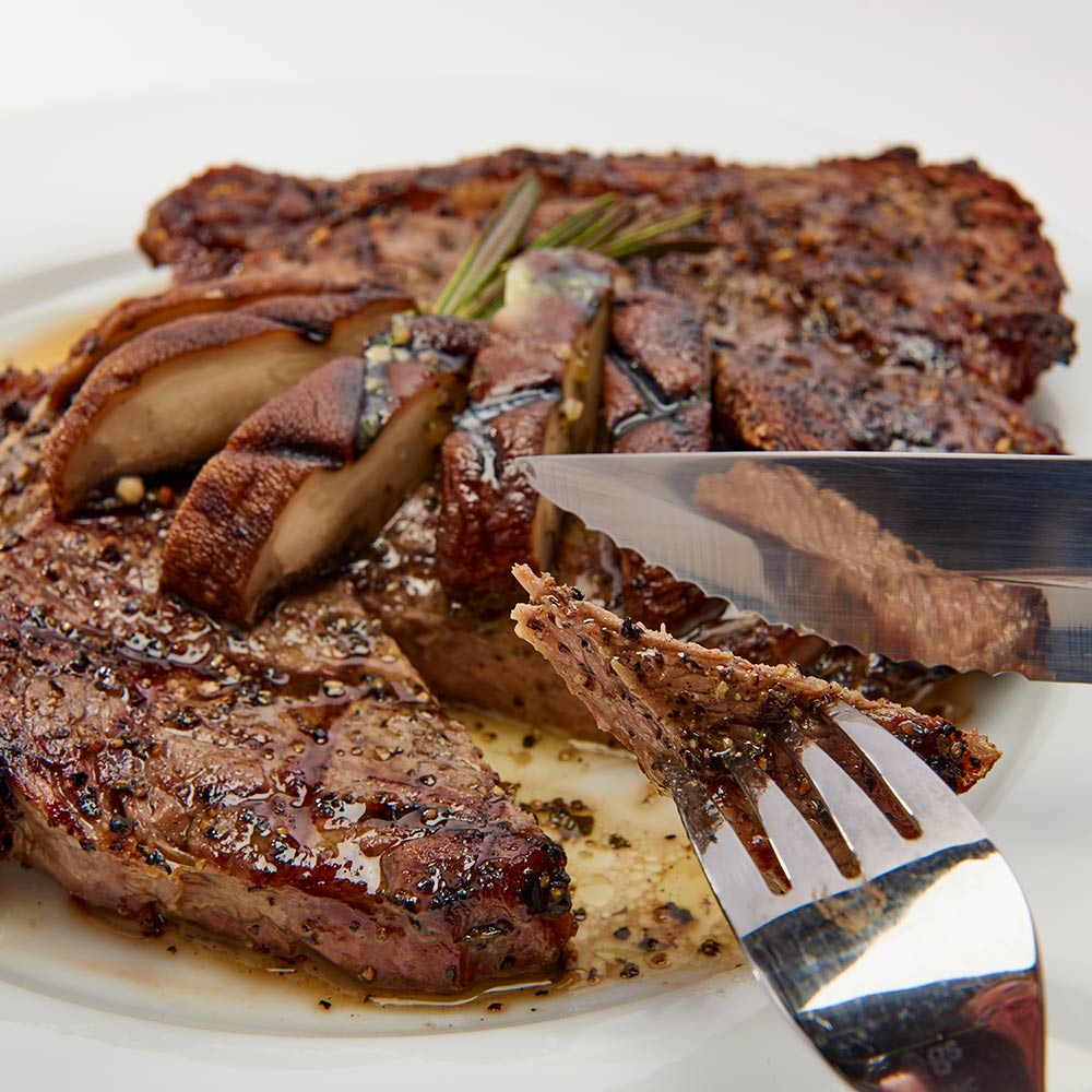 Steak knife with black handle cutting grilled steak on a plate