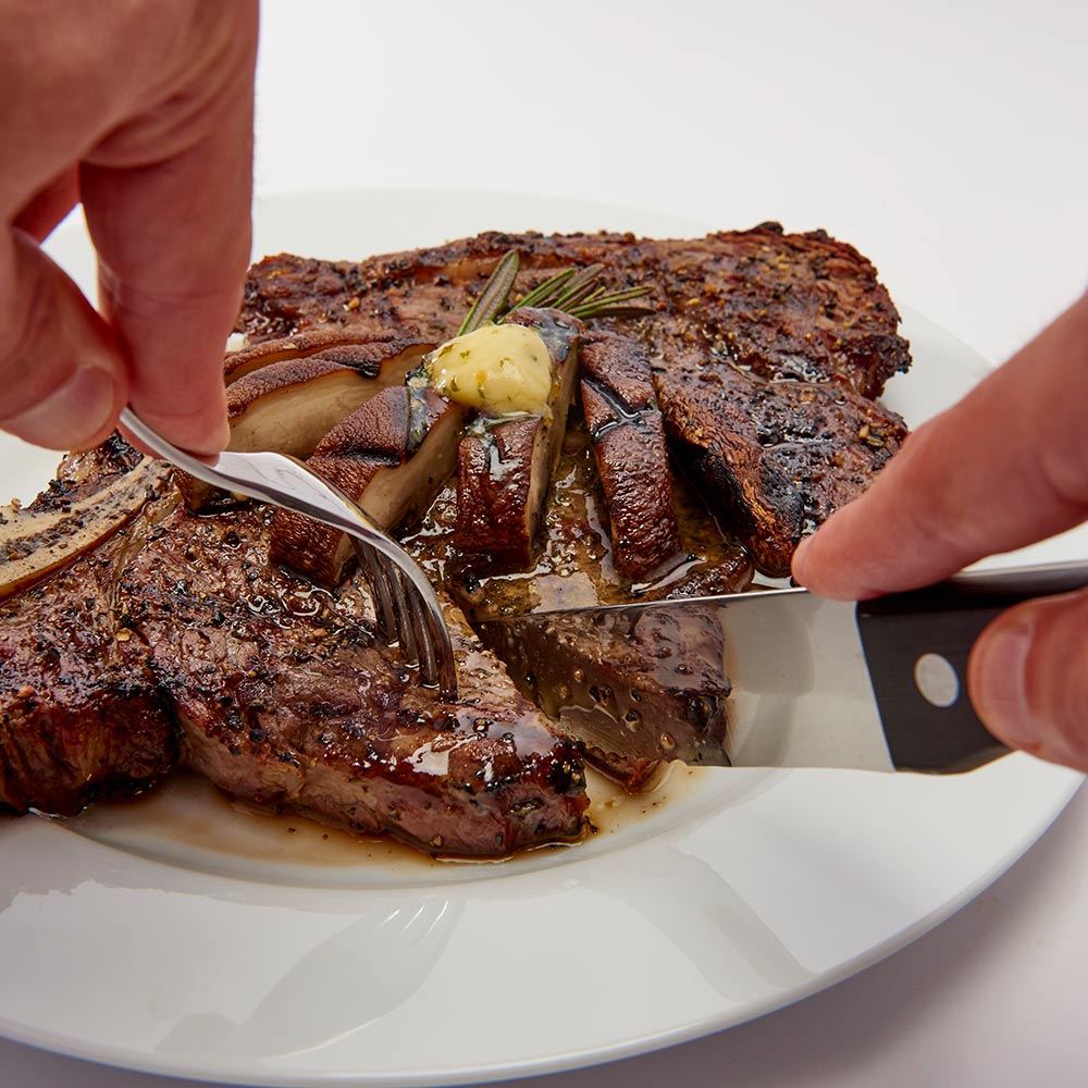 Steak knife with black handle and serving fork handling grilled steak on plate