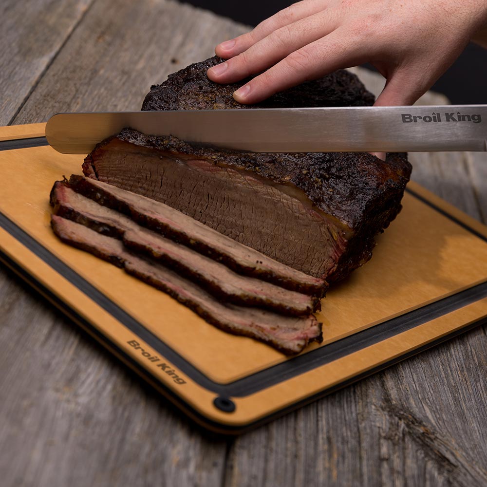 Carving knife slicing brisket on a board, thick meat slices visible
