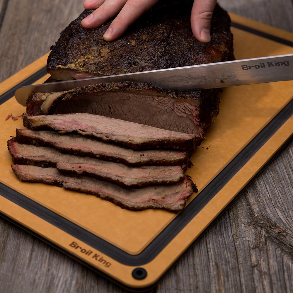 Carving knife over stacked brisket slices on an orange-brown cutting board