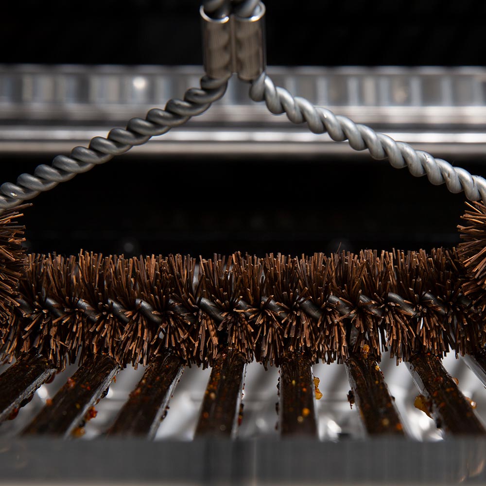 Tri-head grill brush head with dense brown bristles along grill grate bars