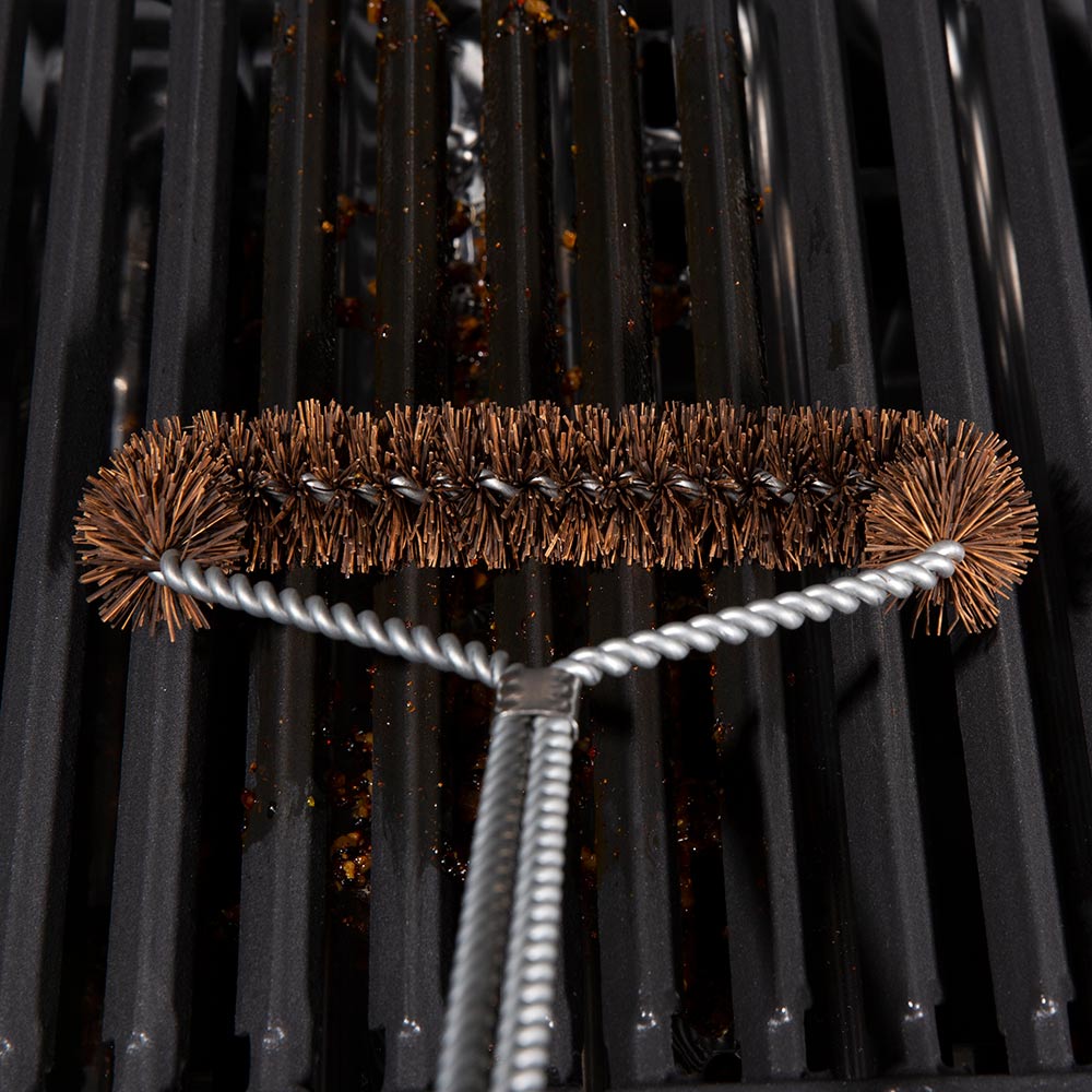 Tri-head grill brush resting on dark grill grates, copper bristles with silver wire