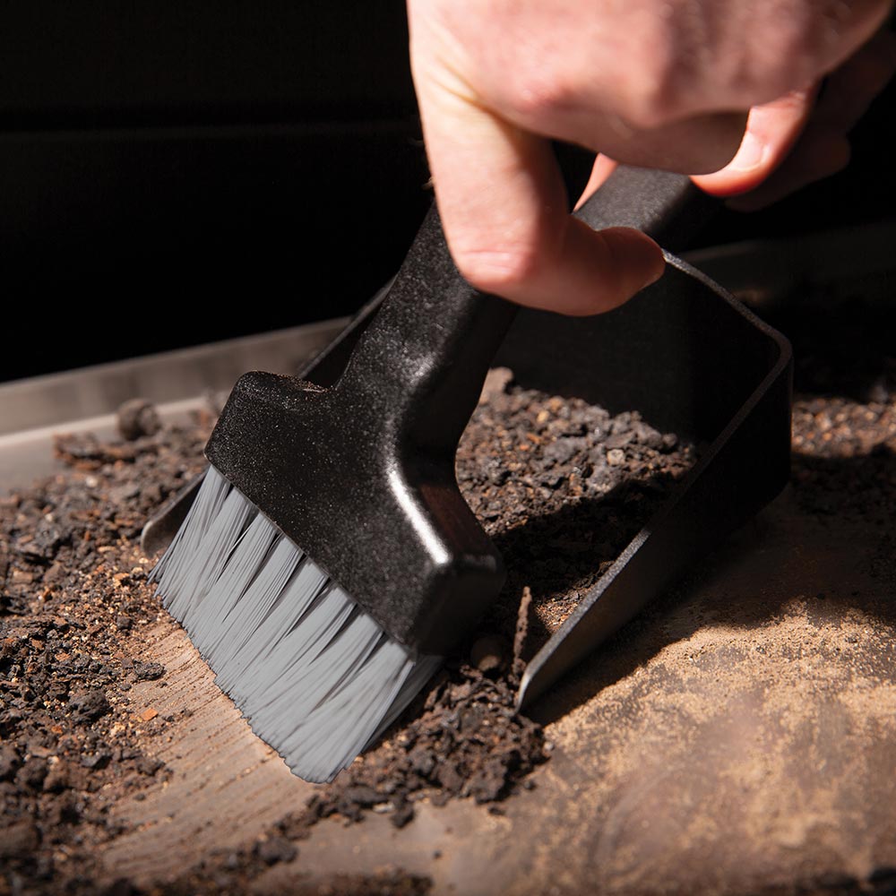Pellet grill brush sweeping ash from metal grate with black handle