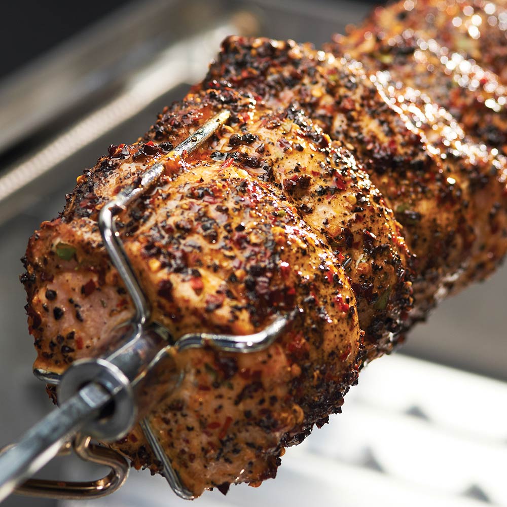 Close-up of rotisserie-roasted meat on metal spit, coated with seasoning
