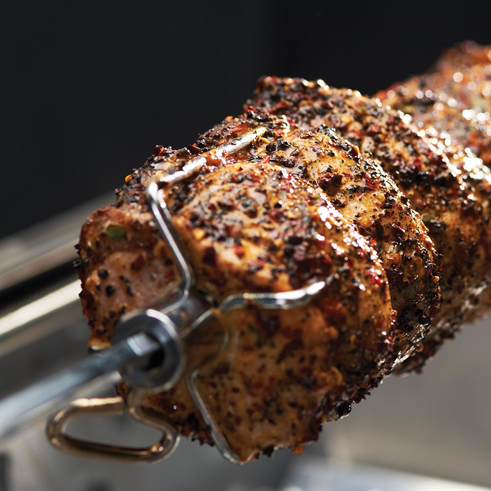 Close-up of rotisserie meat on forks and metal spit inside grill