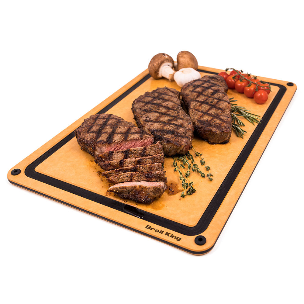 Broil King wood fiber cutting and serving board with grilled steaks, tomatoes, and herbs