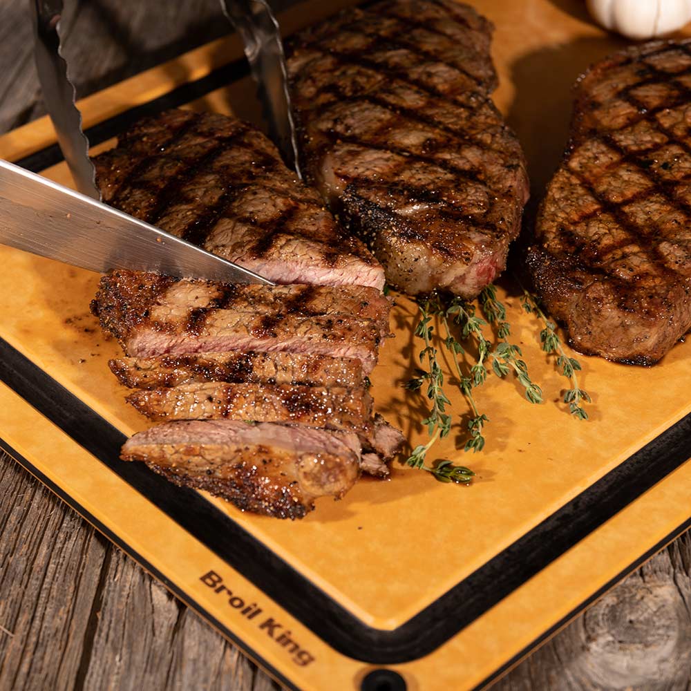 Wood fiber cutting board with sliced grilled steaks and sprigs of herbs