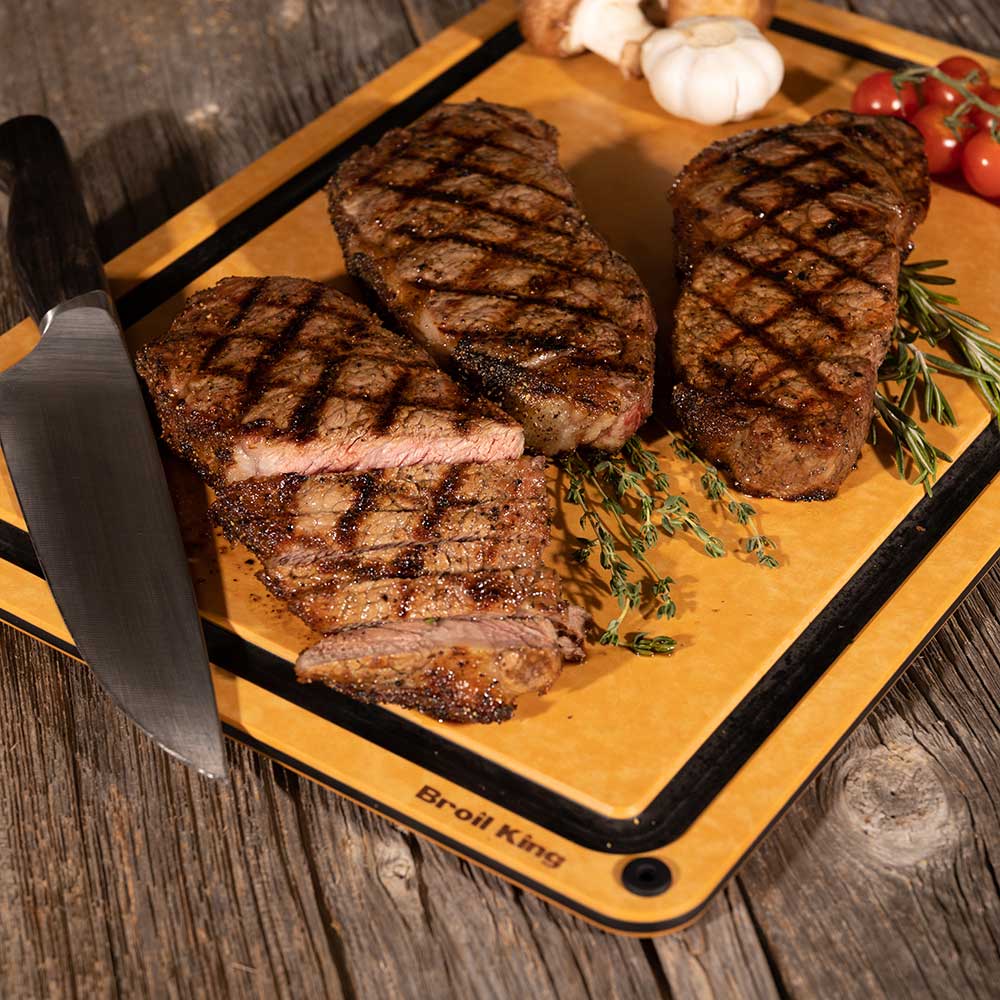 Wood fiber cutting board holding grilled steaks with herbs and cherry tomatoes