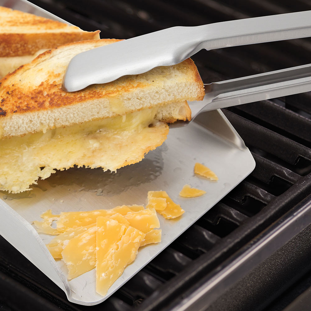 Narrow stainless steel griddle on grill grate with sandwiches and melted cheese