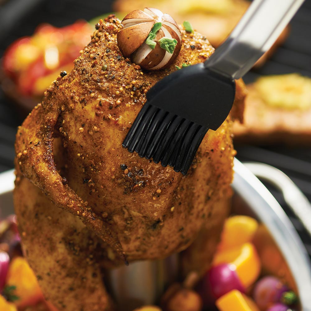 Stainless steel chicken roaster pan with seasoned chicken and basting brush