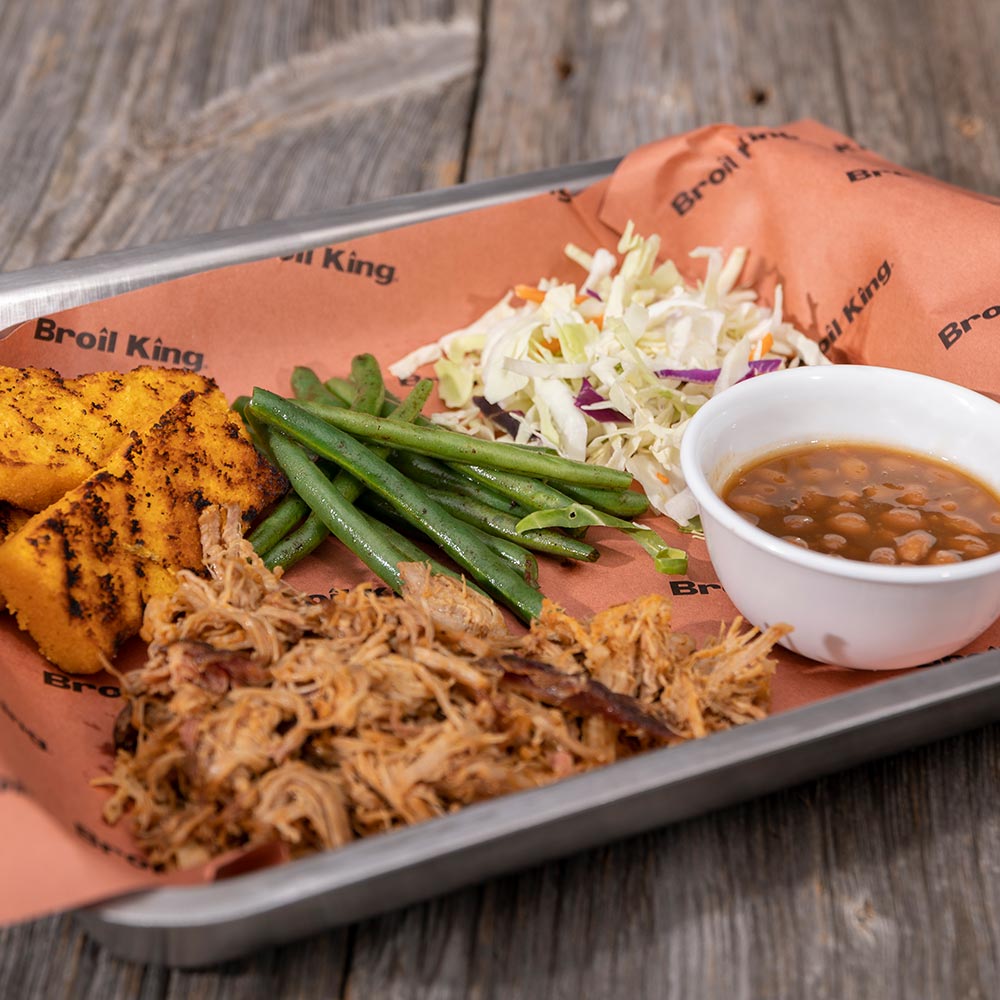 Butcher paper-lined tray with pulled meat, green beans, shredded slaw, and sauce cup