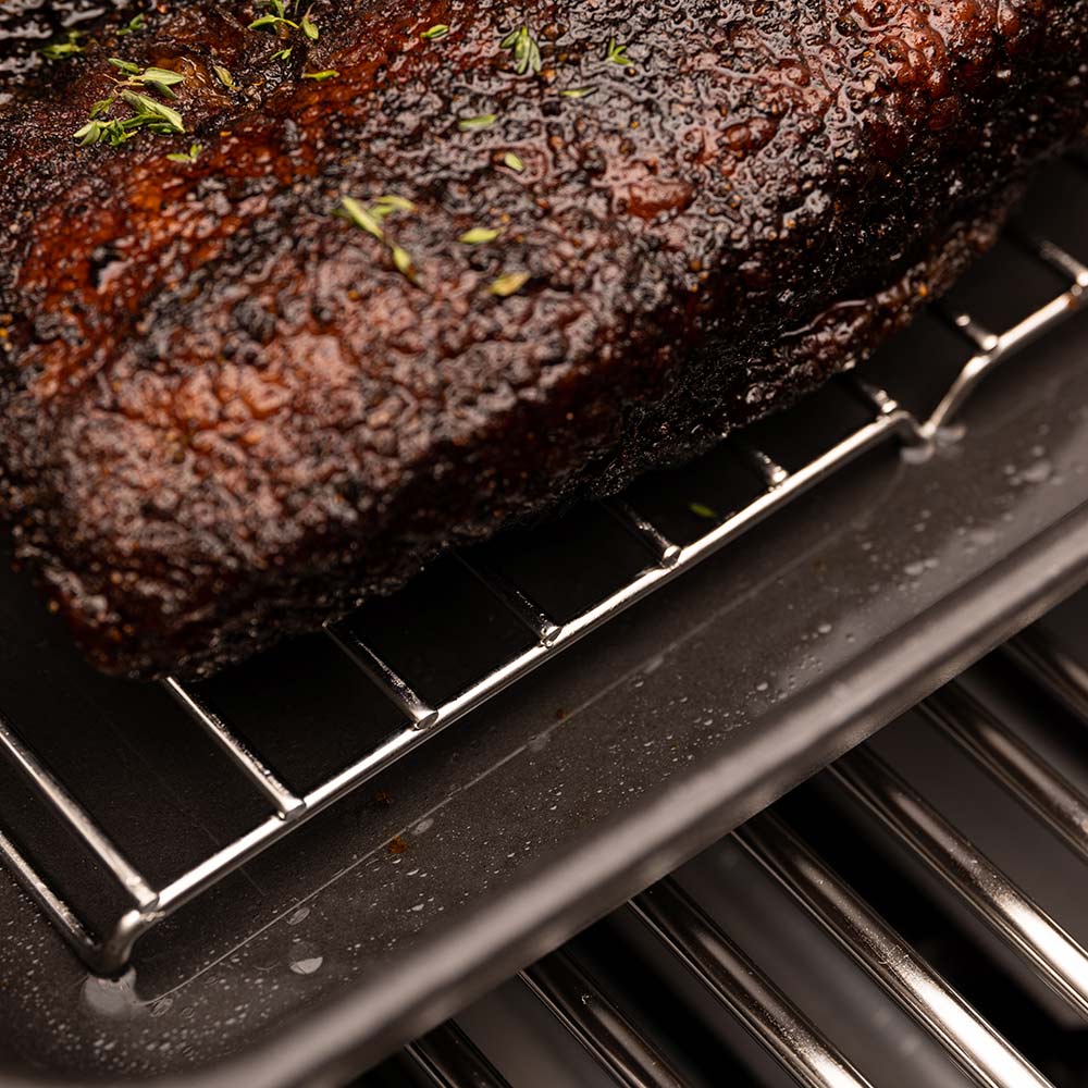 Cast iron multi roaster with seared roast on rack, close view of grill bars