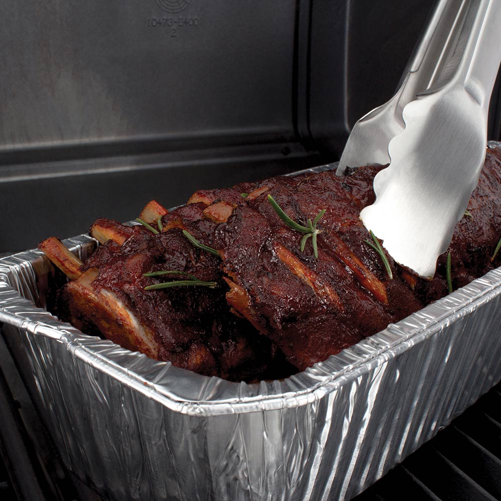 Aluminum foil roaster liner holding cooked ribs with metal tongs