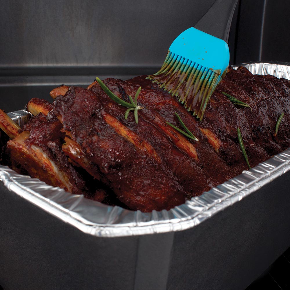 Aluminum foil roaster liner with cooked ribs being brushed with sauce