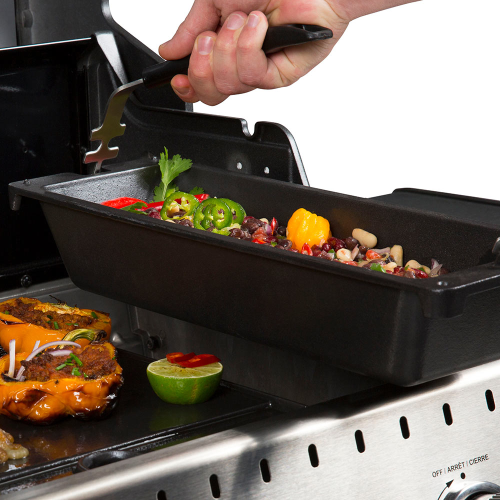 Cast iron rib roaster on grill with peppers and herbs, lid lifted by hand