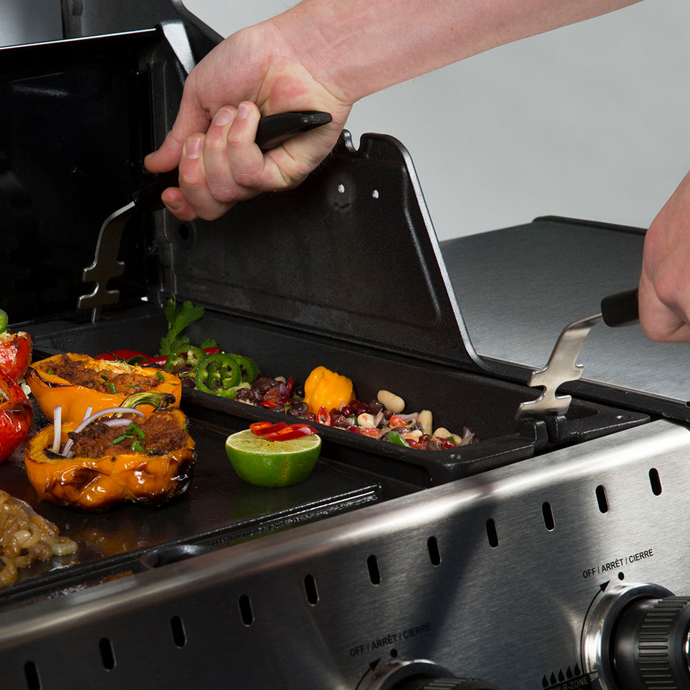 Hand opening grill lid beside cast iron wok tray with cooked food