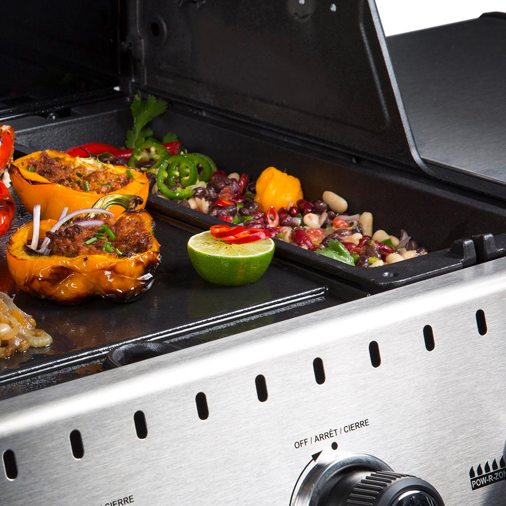 Cast iron rib roaster on grill with peppers and cooked meat, lid partially open