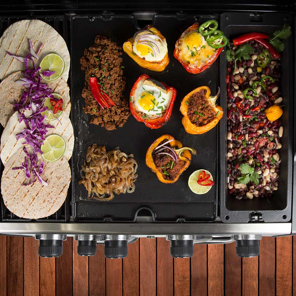 Cast iron wok insert on grill with sliced onions, peppers, and eggs cooking