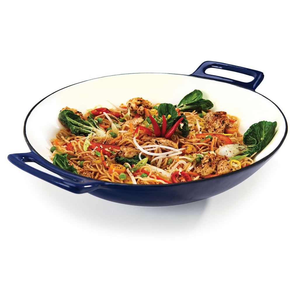 Porcelain cast iron wok with blue handles, filled with noodle stir-fry and greens