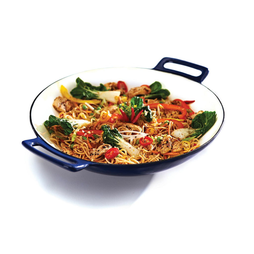 Porcelain cast iron wok with two blue side handles, filled with noodle and pepper stir-fry