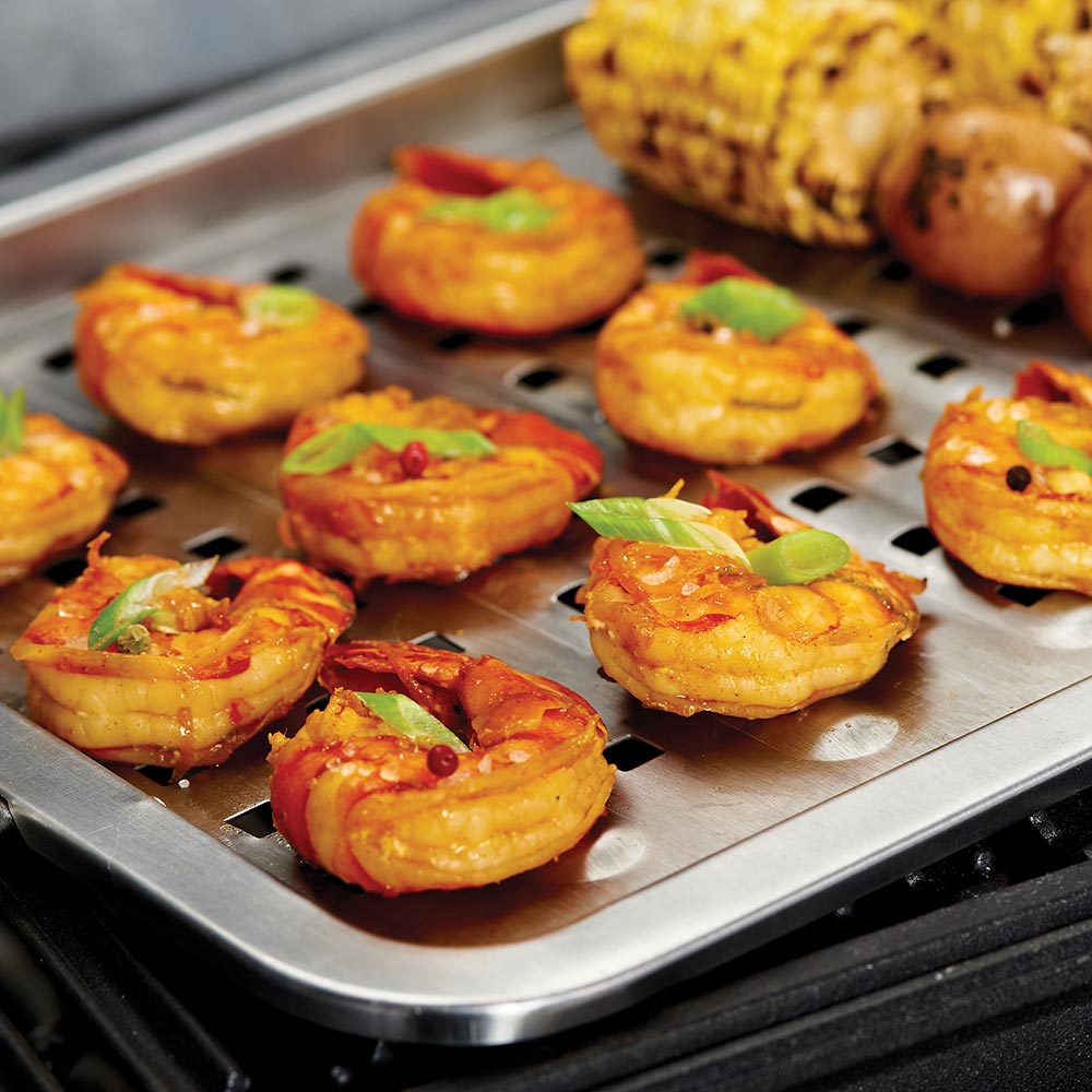 Perforated stainless steel grill topper surface with vegetables and sausages cooking