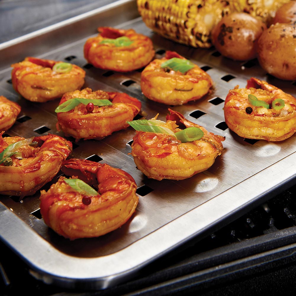 Perforated stainless steel grill topper with grilled slices and sausages on top