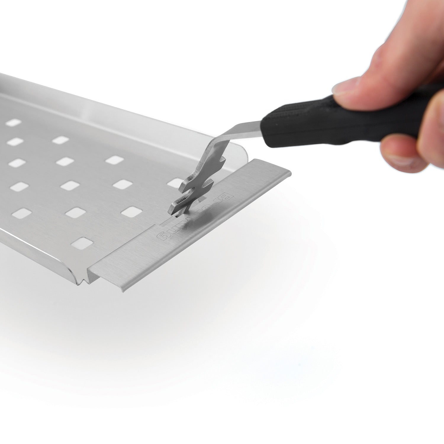 Stainless steel grill topper tray being snapped into place with a forked tool