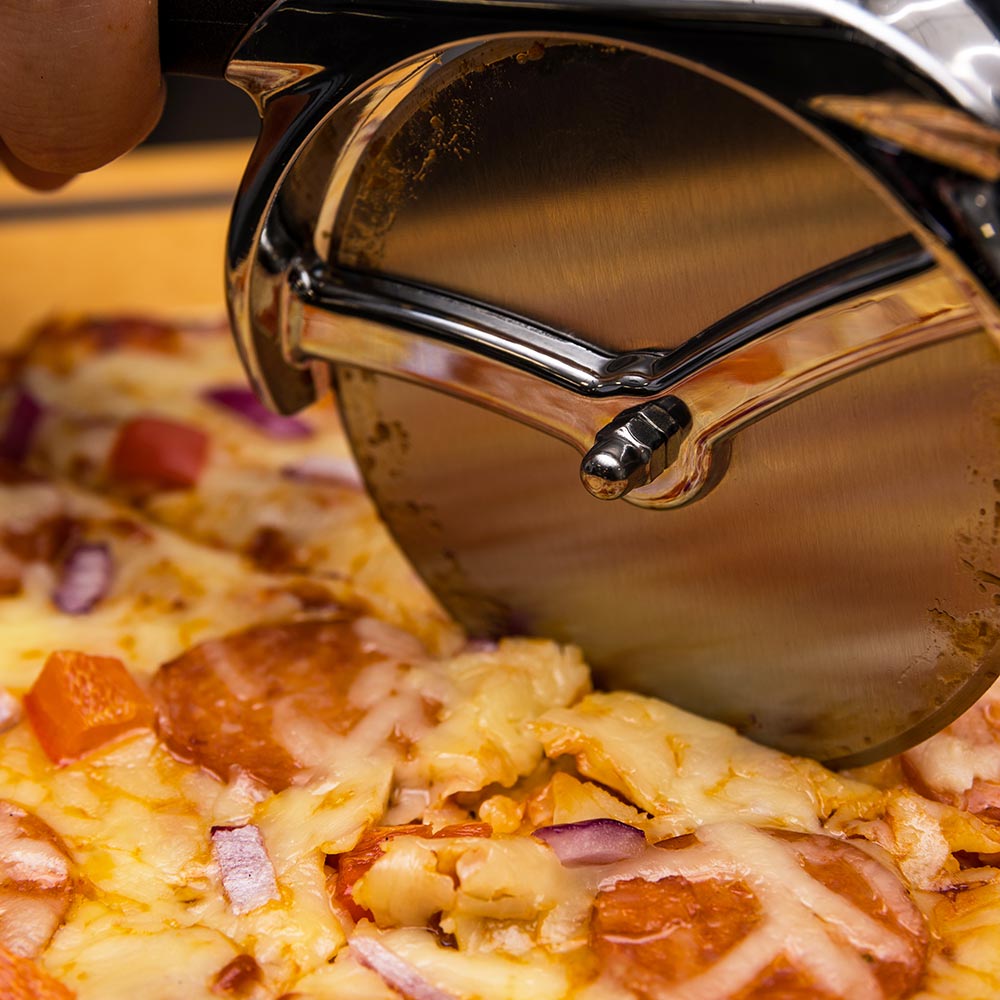 Close-up of chrome pizza cutter wheel pressing through cheese and toppings
