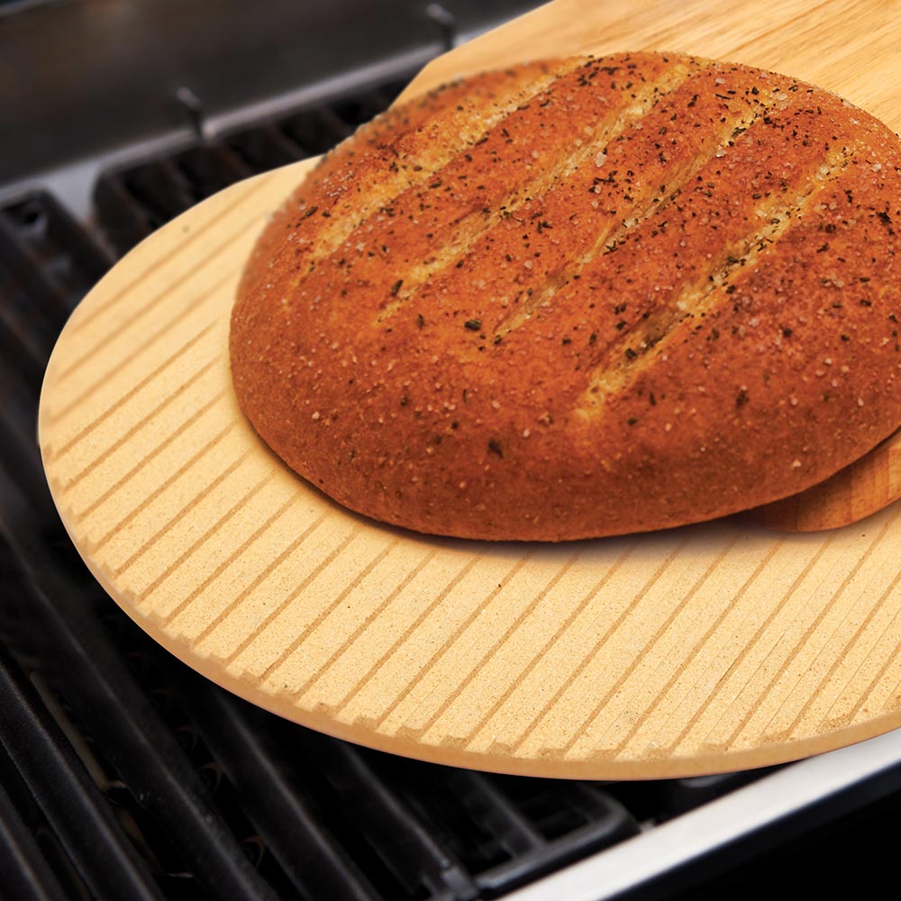 Round tan grilling stone with seasoned pizza crust on grill grates