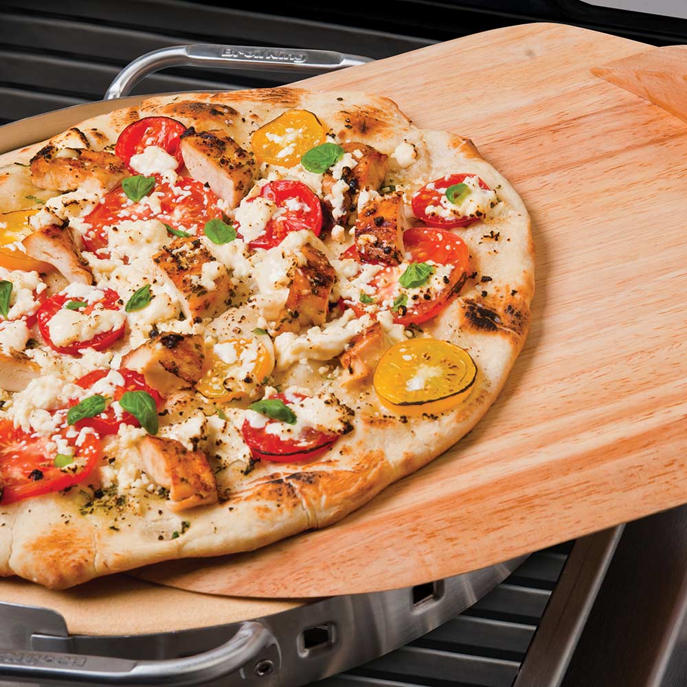Pizza stone grill set with pizza on wood peel over the stone