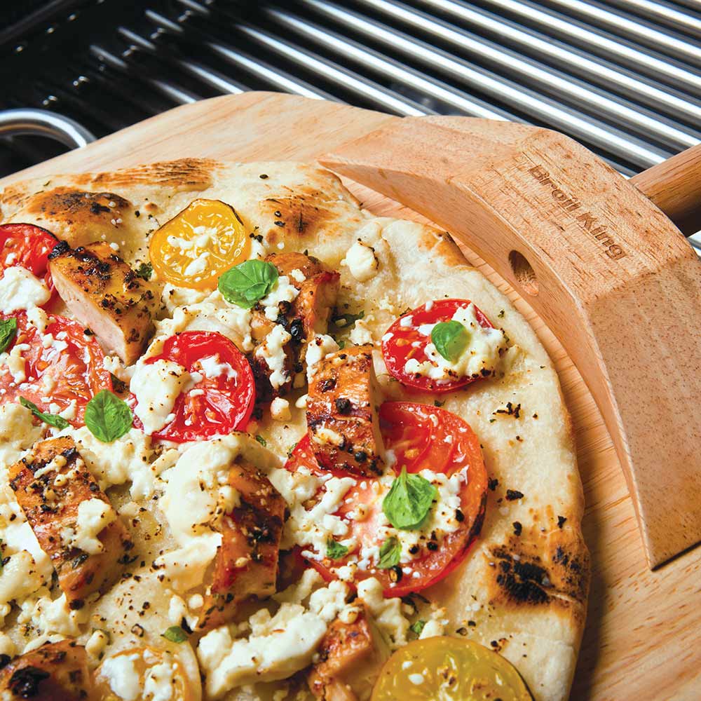 Pizza on circular stone grill set with wooden peel and grill grates
