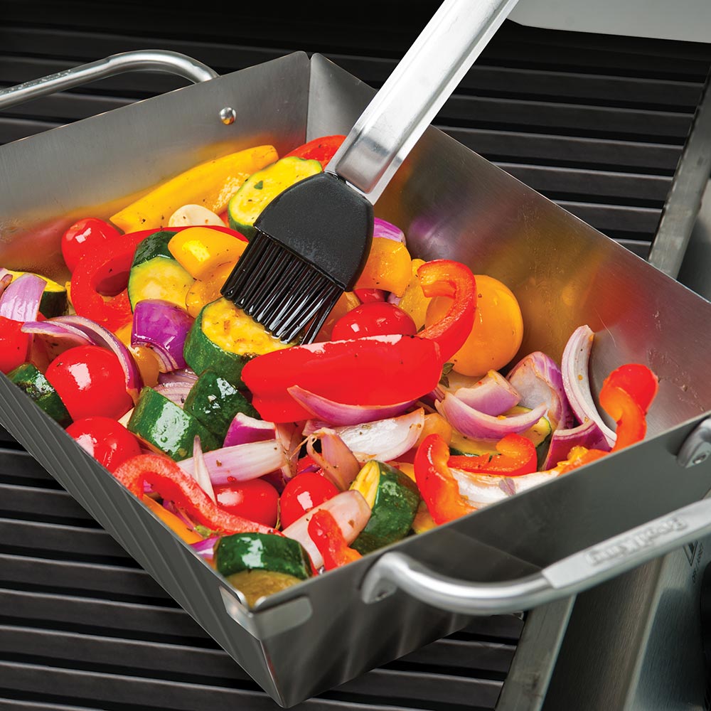 Stainless steel wok with peppers and onions on a grill grate