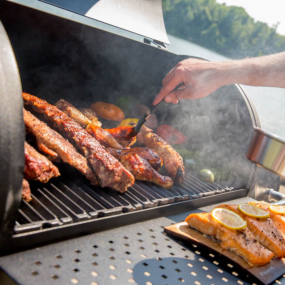Smoker grates with assorted grilled meats and smoke rising from food
