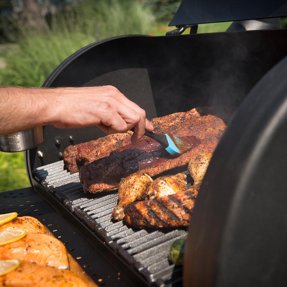 Charcoal smoker with person placing meat on the grill grate with a blue utensil