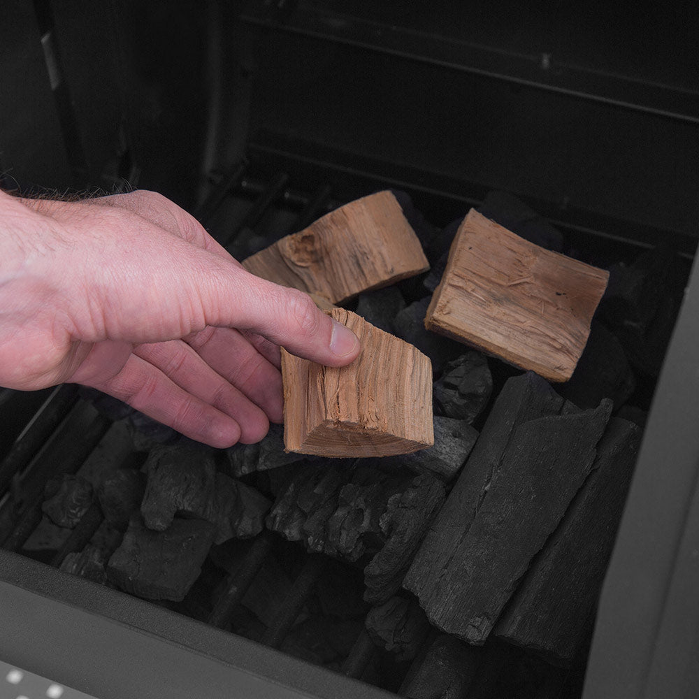 Hand adding wood chunks into the smoker firebox fuel tray