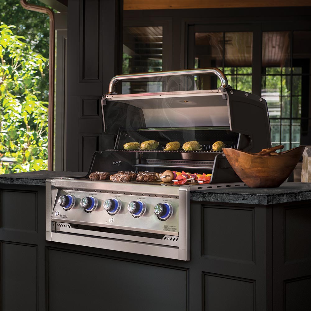 Stainless steel 5-burner built-in gas grill with lid open, grilling food inside