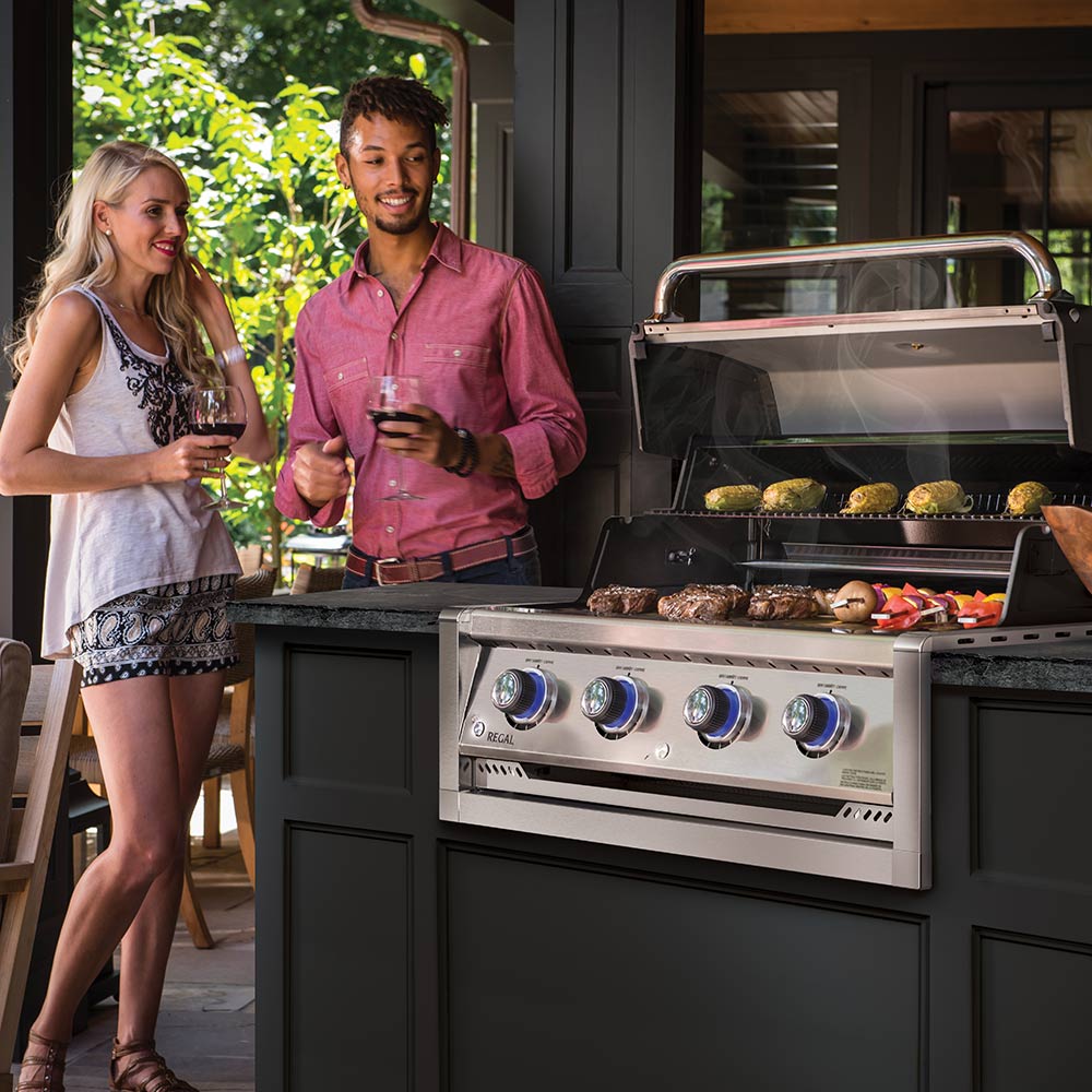 Built-in gas grill head with open lid and food on the cooking grates, front view