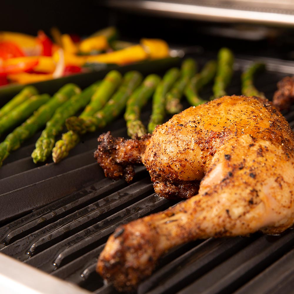 Grill grates with chicken and green peppers cooking, close-up from above